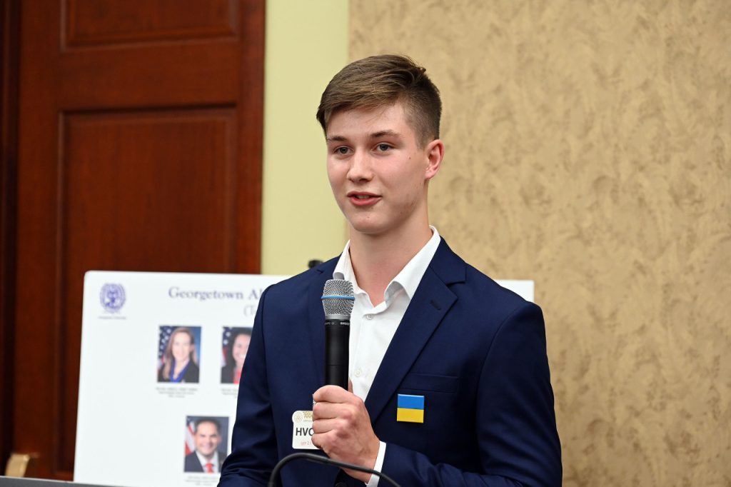 Young man with a Ukraine flag pinned on his blazer speaks into a microphone