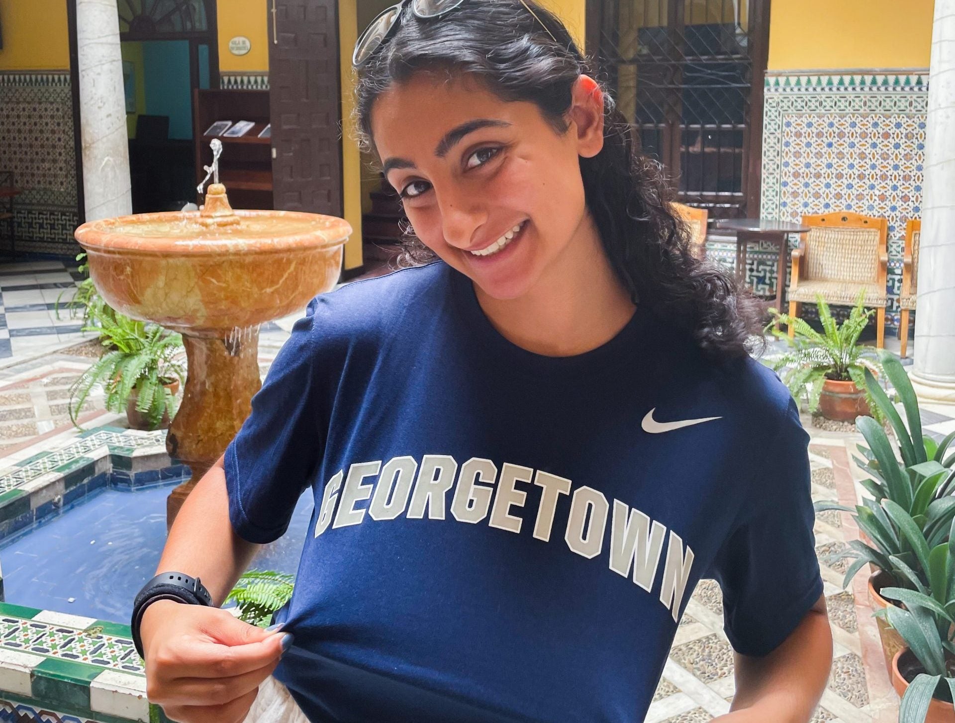 Young woman wearing a blue Georgetown T-shirt holds it out to display the "Georgetown" graphic