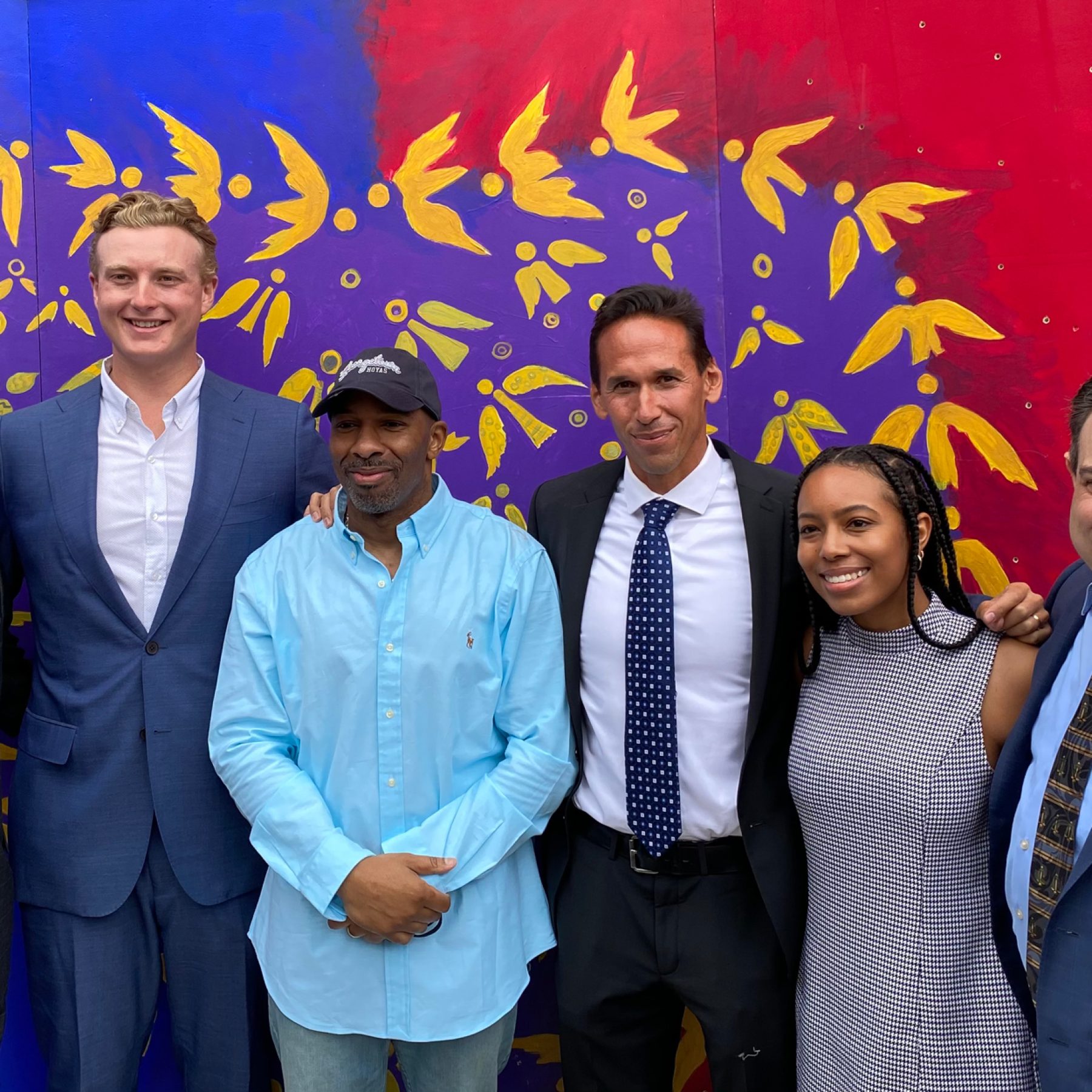 Students with Eric Riddick and Professor Marc Howard in front of a blue and red background with a purple and yellow heart in the middle