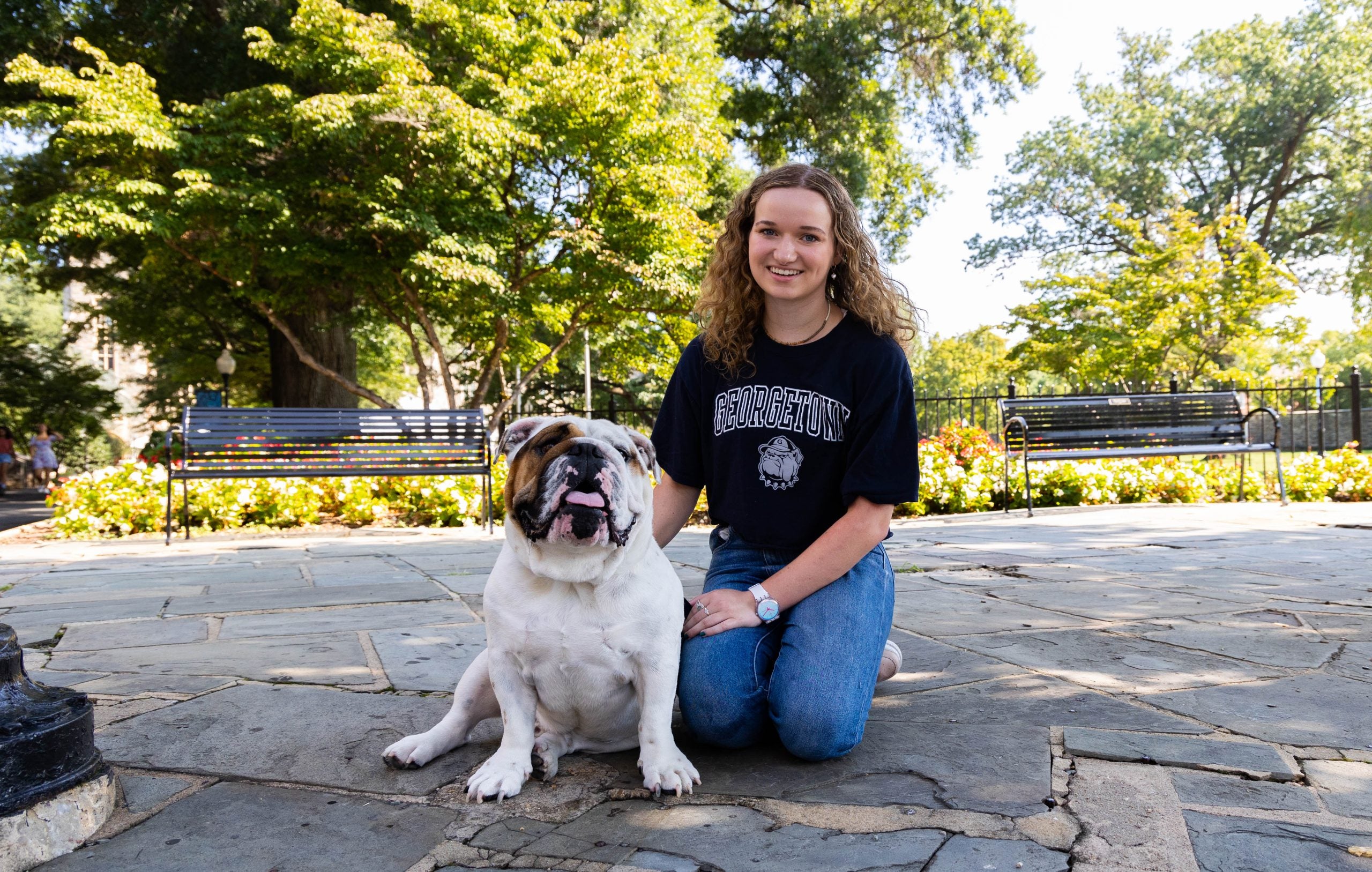 Young woman wears a dark blue Georgetown T-shirt while kneeling next to Jack the Bulldog