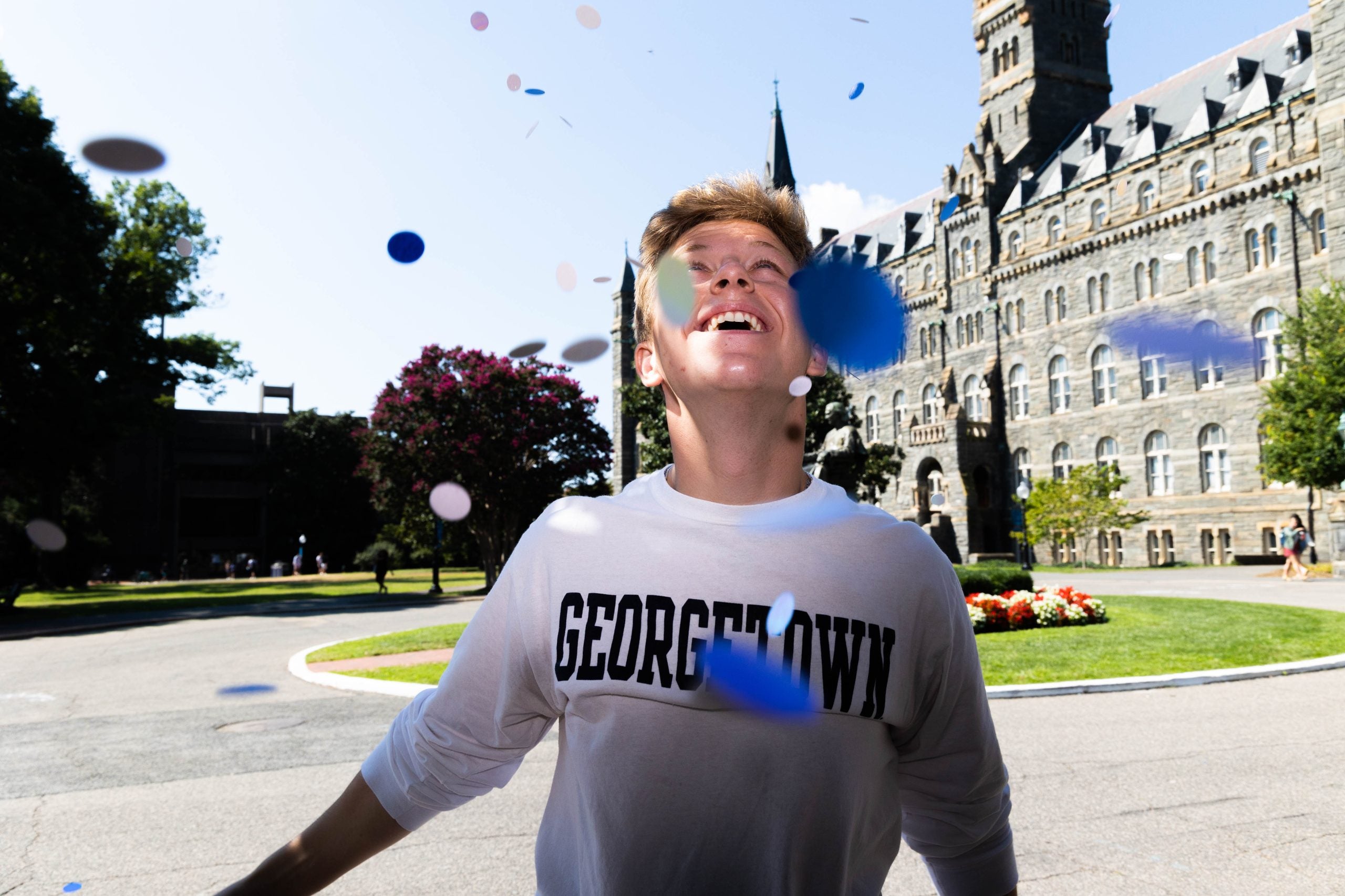 Young man wearing a gray Georgetown sweatshirt looks up at confetti outside