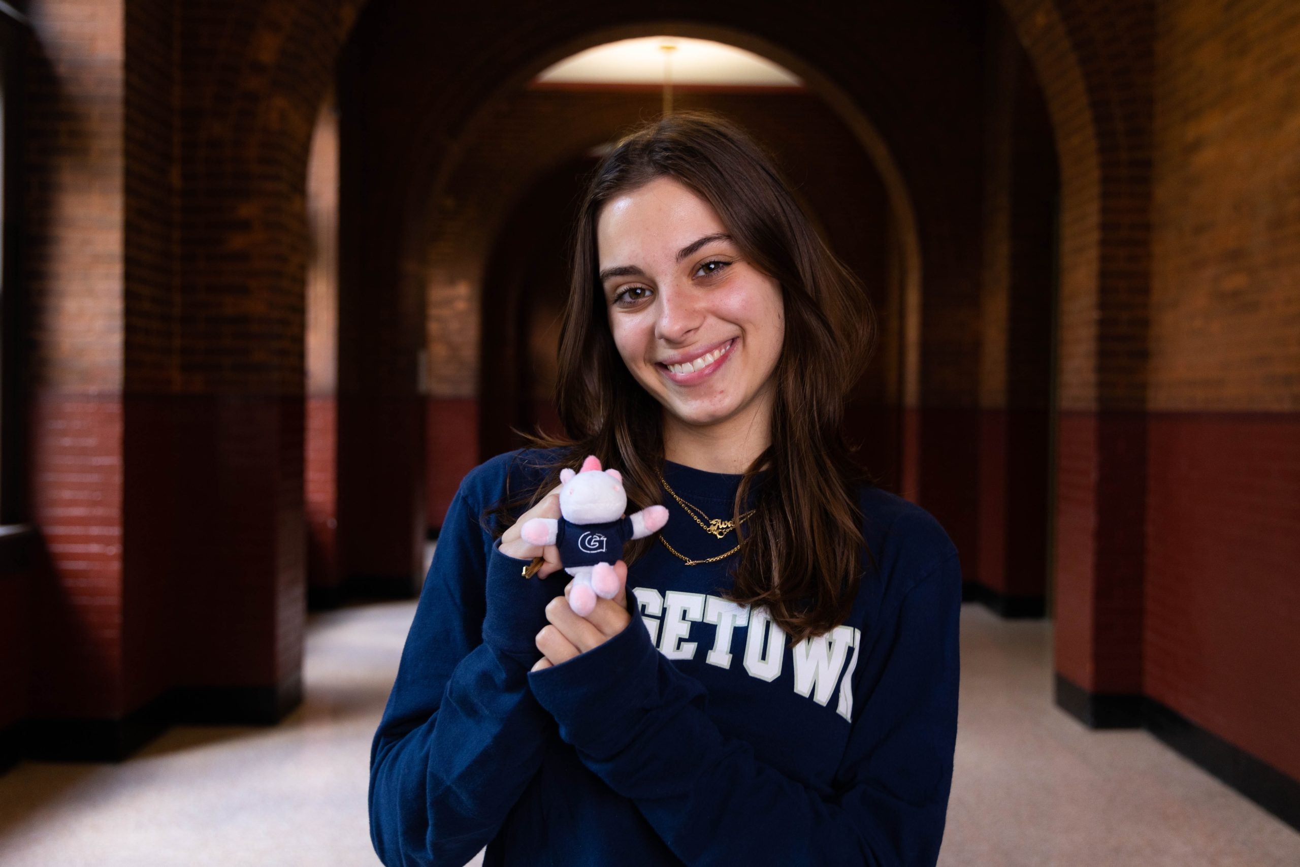 Young woman wearing a blue Georgetown sweatshirt holds a small Jack the Bulldog stuffed animal