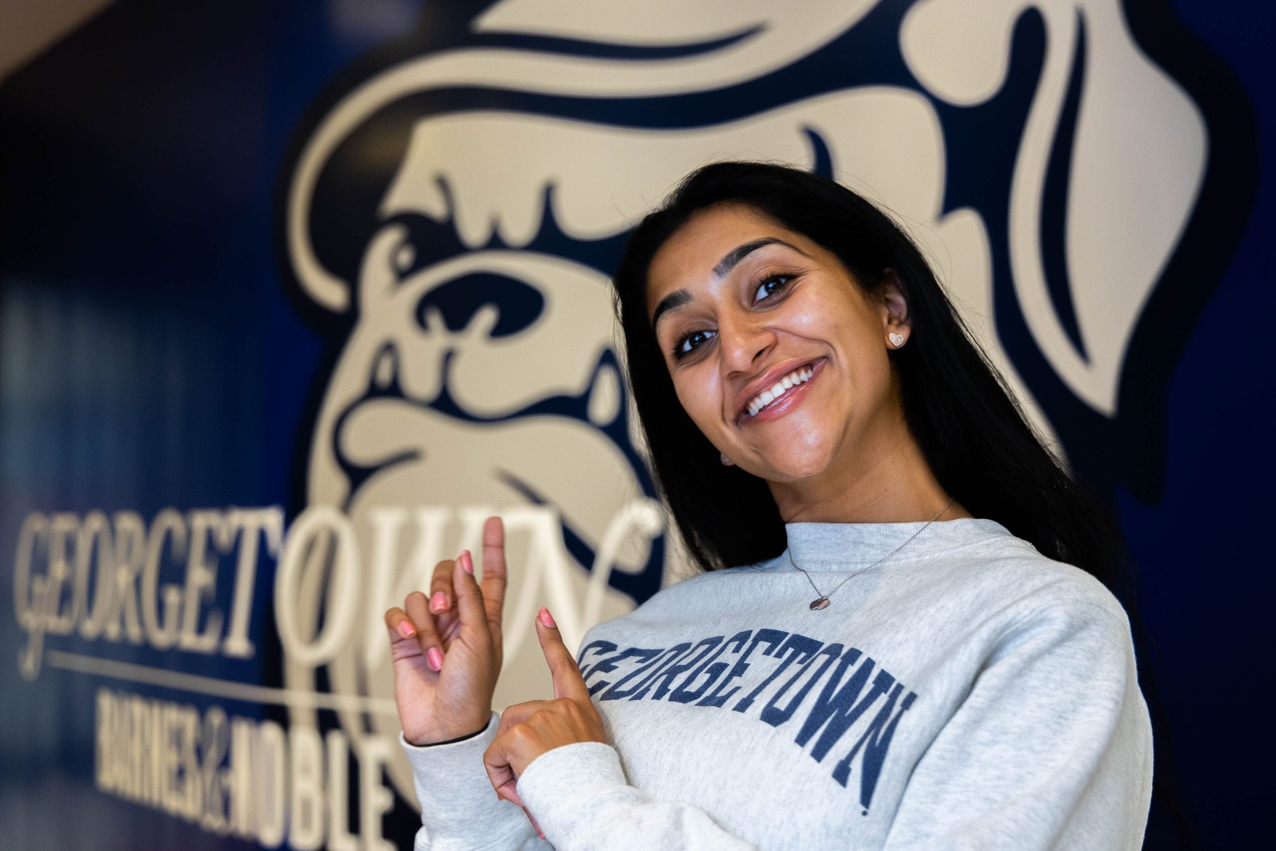 Young woman in a gray Georgetown sweatshirt points to a wall mural of Jack the Bulldog