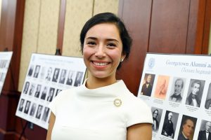 Majeda Abu-Alghanam wears a white blouse in front of signs with headshots of Hoyas who served in Congress