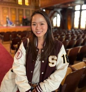 Young woman in a letterman jacket stands in an empty Healy Hall