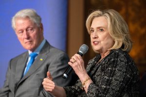 Hillary Clinton speaks into a microphone while Bill Clinton listens