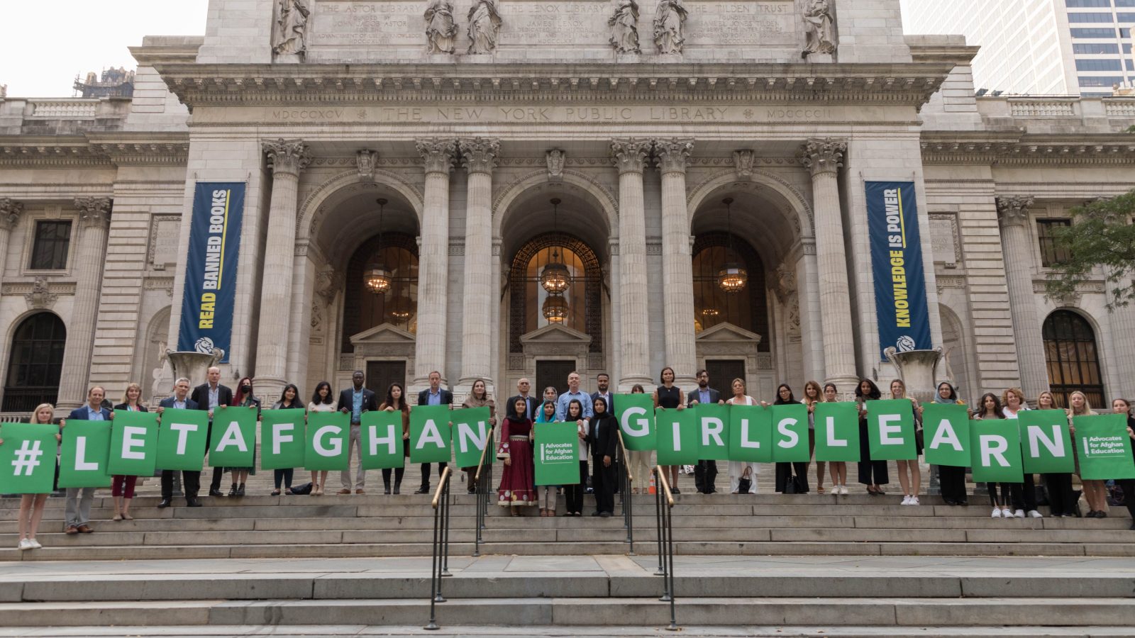 Women holding individual signs with green letters in front of an old building spelling out 