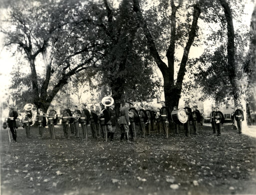 The Georgetown Pep Band, dressed in military regalia, stands in a field by trees in 1932. The black-and-white photo also shows the side of a snare drum that says "ROTC"