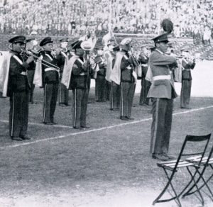 The Georgetown Band plays at a football game in 1942 in this black-and-white photo. They are wearing blue and gray trousers and waist-high capes.