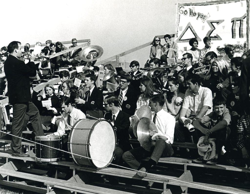 A black-and-white photo of the band sitting in the stands of a game and playing their instruments