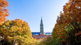 An image of fall leaves on trees surrounding a tower with a bright blue sky in the background