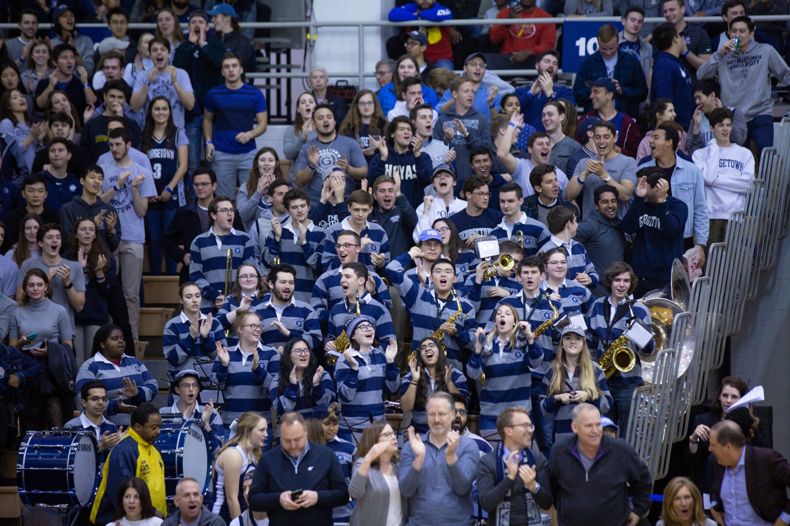 Members of the Georgetown Pep Band stand in the bleachers at a men's basketball game cheering on the team.