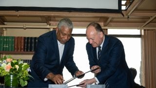 Georgetown&#039;s president (right) and the president of the Southern University System (left) sign a memorandum of understanding on a blue table in a library.