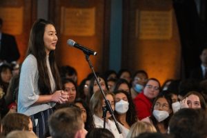 Young woman stands in front of a microphone in the middle aisle of an audience