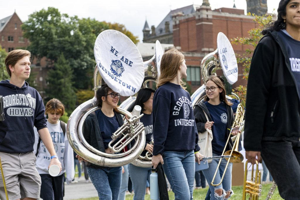 Members of the Georgetown Pep Band walk together while carrying their instruments, including a sousaphone and a tuba
