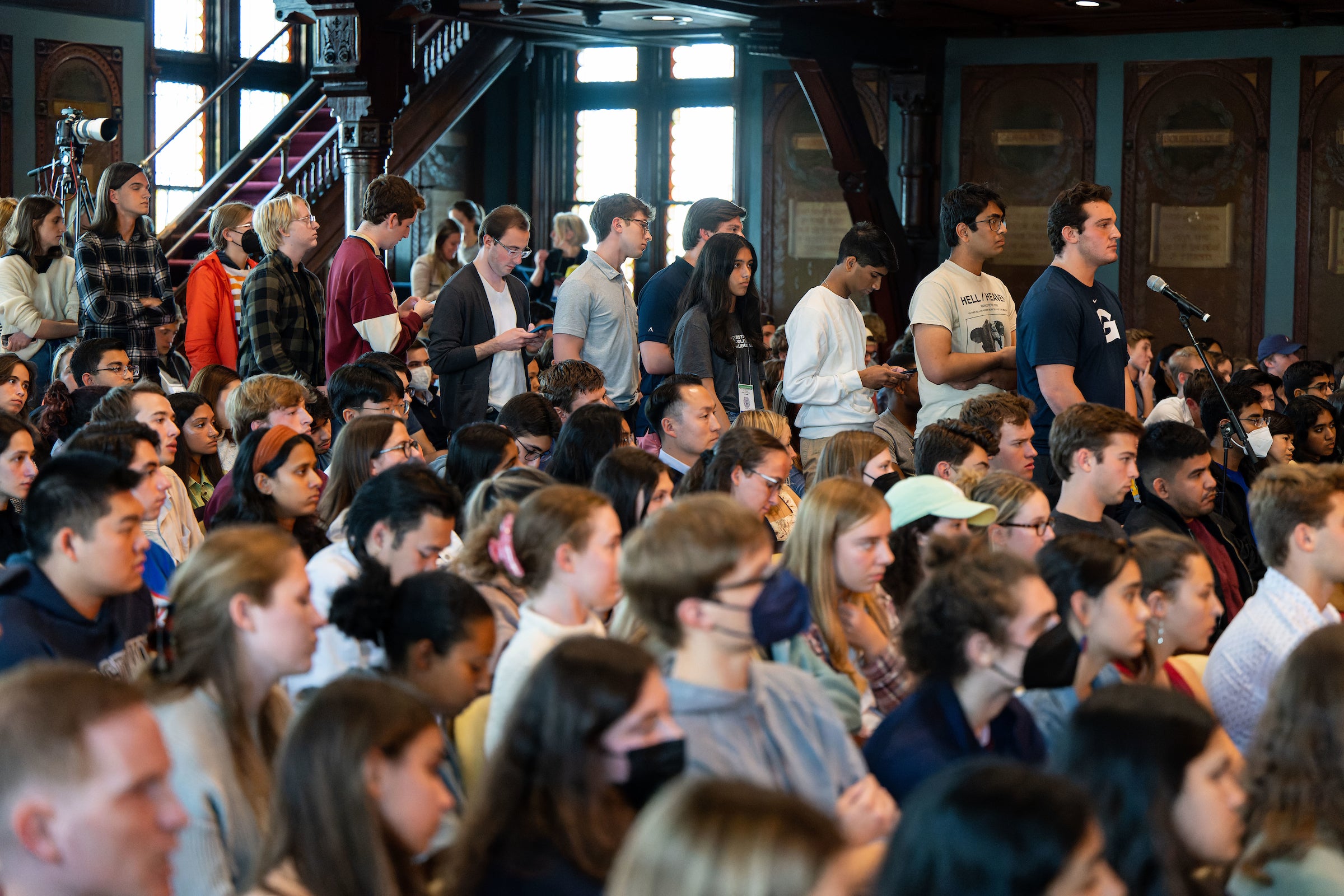 Students line up behind a microphone to ask questions in a crowded audience