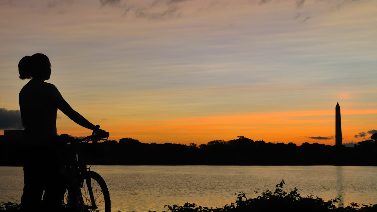 Bicyclist looks across Potomac River at the Washington Monument at sunrise