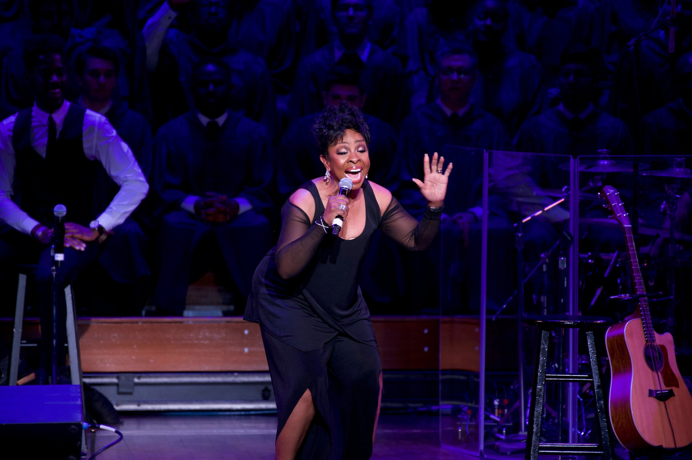 Gladys Knight holds her hand up and closes her eyes as she sings into a microphone onstage