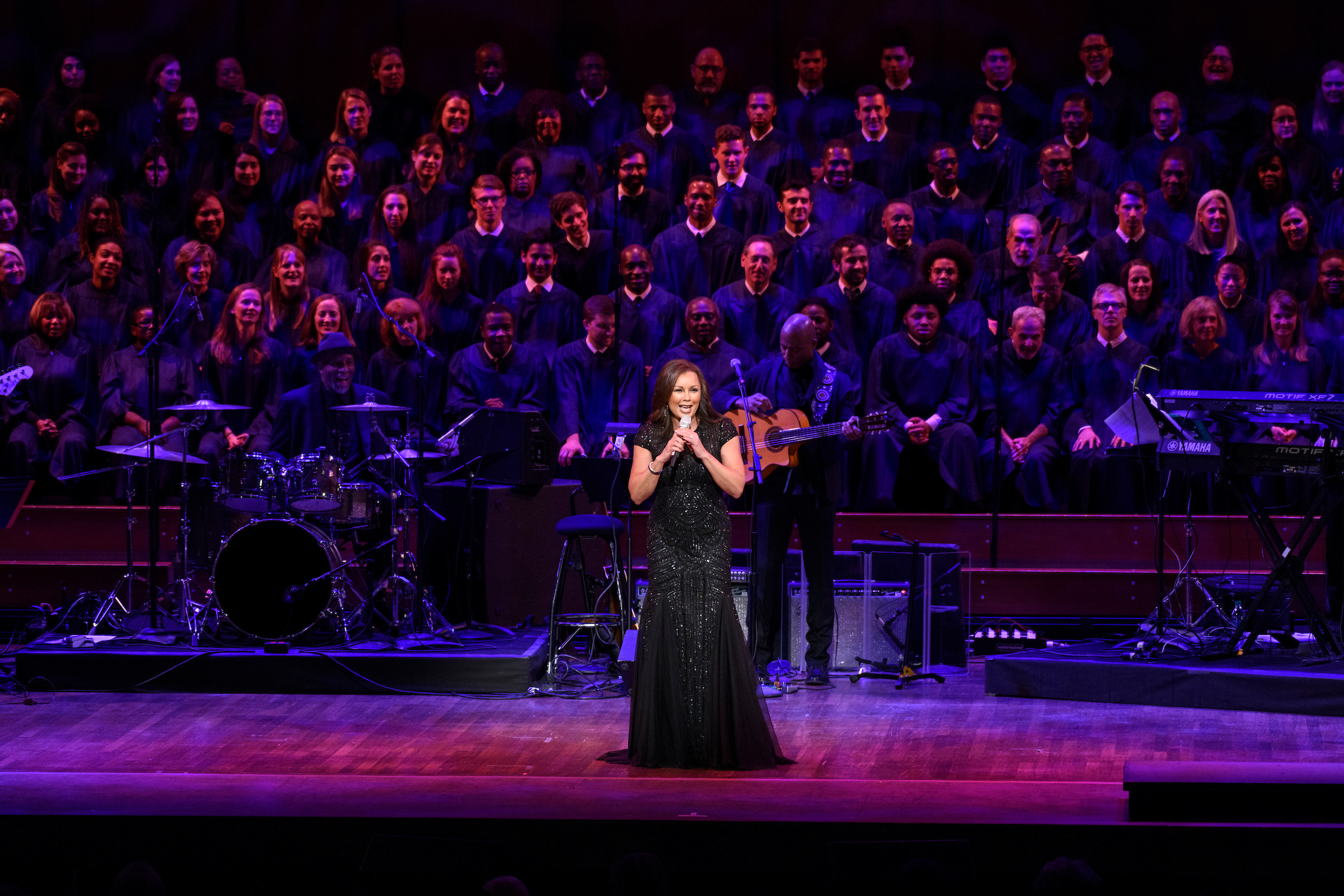 Vanessa Williams wears a long black gown and sings in front of a choir