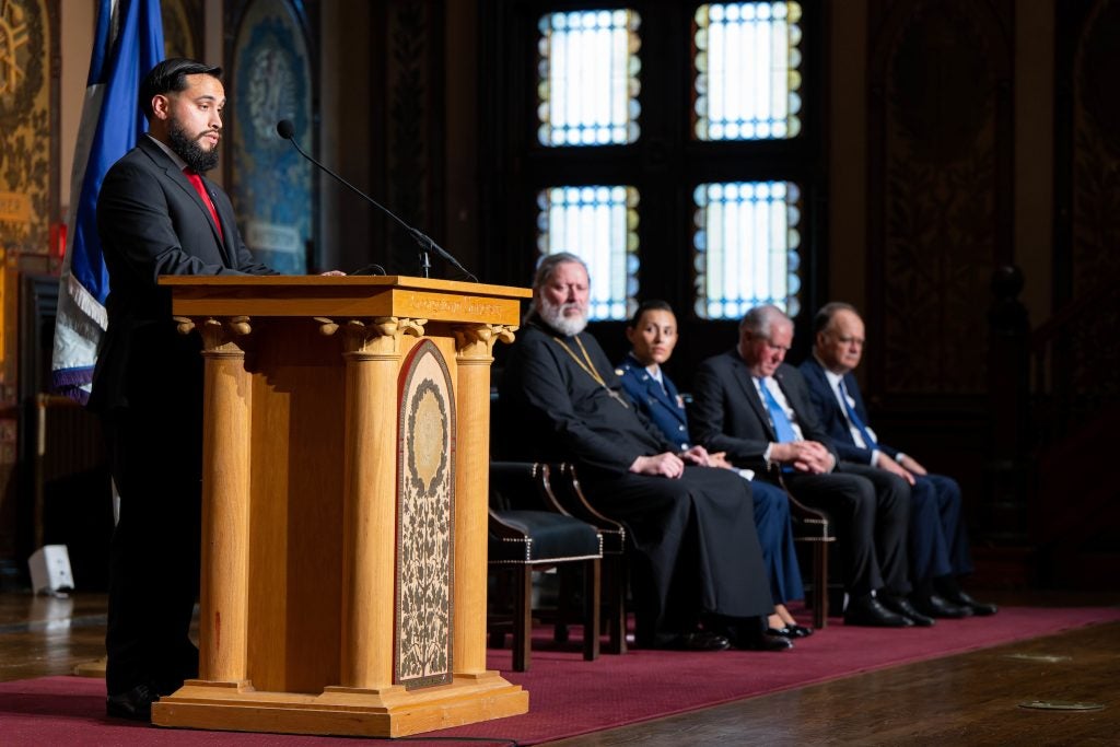 Oswaldo Pazmino speaks from behind a podium while panelists onstage watch his speech