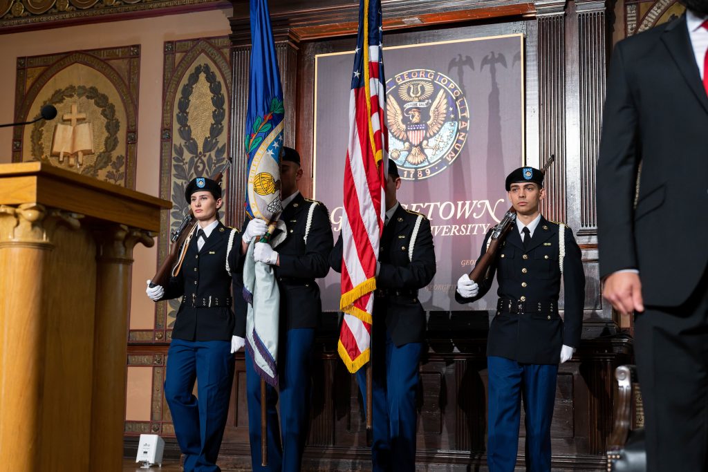 Students in military uniforms hold flags and rifles