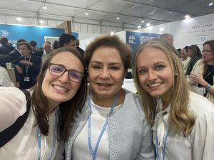 Three women in cream-colored shirts pose together in a conference room at COP27.