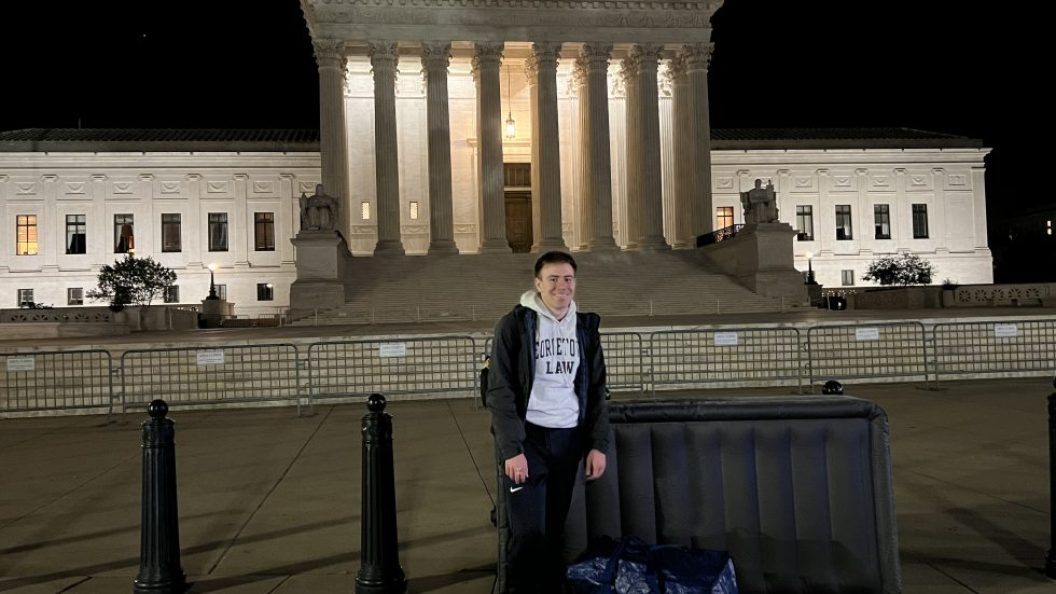 A student stands outside the Supreme Court at night with an air mattress next to him.