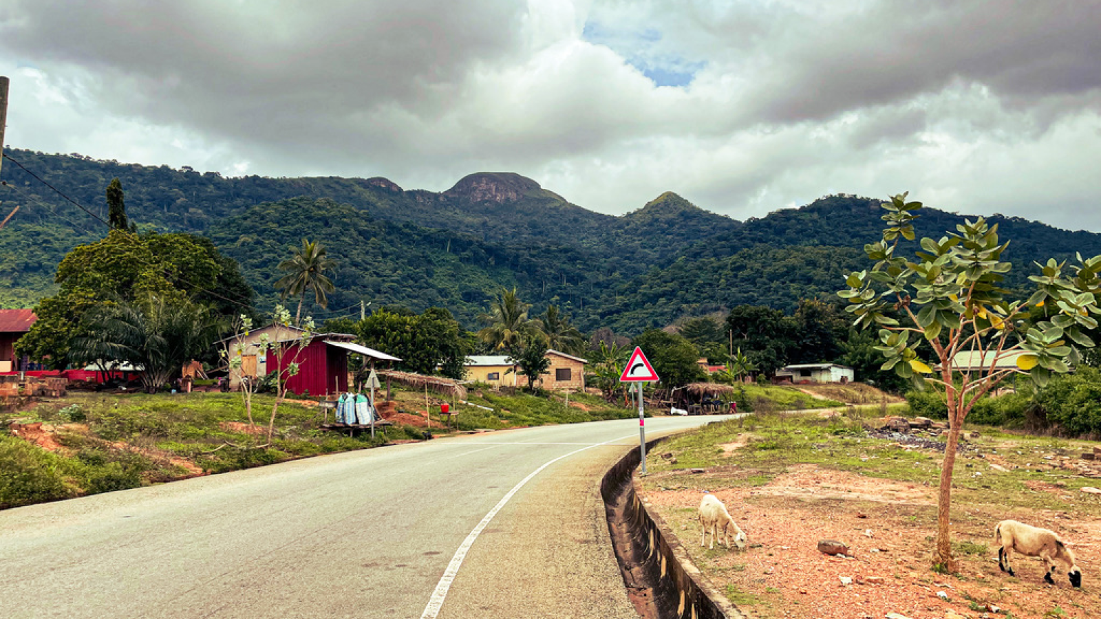 A road curving around a bend with green mountains in the background and red houses along the road