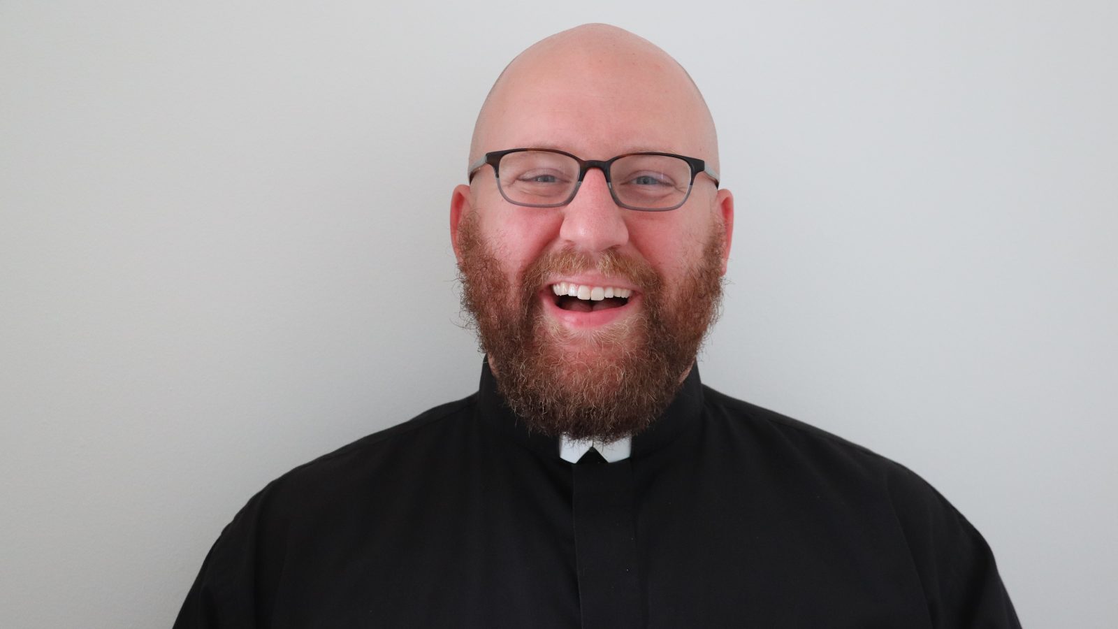 A headshot of Ken Homan (G'25) who is wearing glasses and is dressed in black with a white collar. Ken is a Jesuit brother and part of the Society of Jesus.