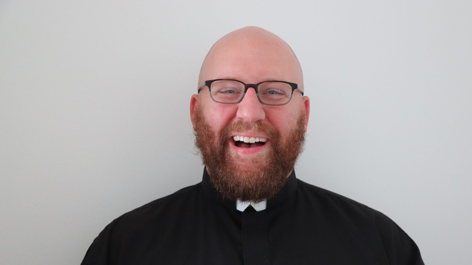 A headshot of Ken Homan (G'25) who is wearing glasses and is dressed in black with a white collar. Ken is a Jesuit brother and part of the Society of Jesus.
