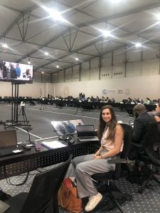 Tessa Ide, a graduate student at MSFS, sits behind a table in a large room where other climate negotiators sit behind long desks.