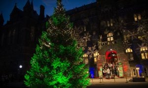 Healy Hall at dusk with lit Christmas Tree and singers on steps.