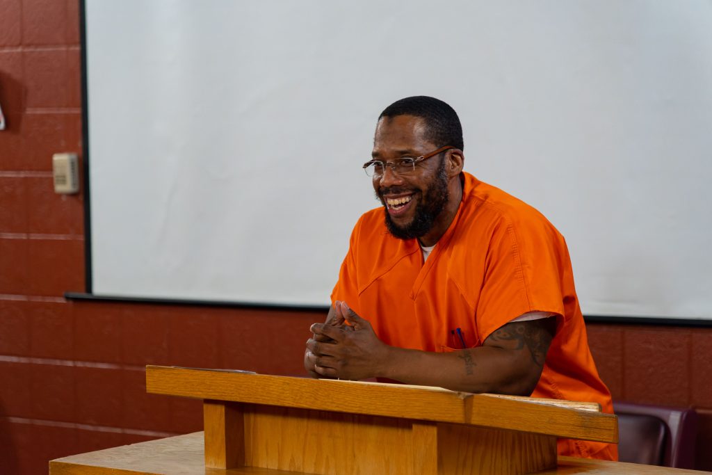 Colie “Shaka” Long speaks behind a podium at the end-of-semester celebration at a DC jail in 2021 while incarcerated. He is wearing an orange jumpsuit. 