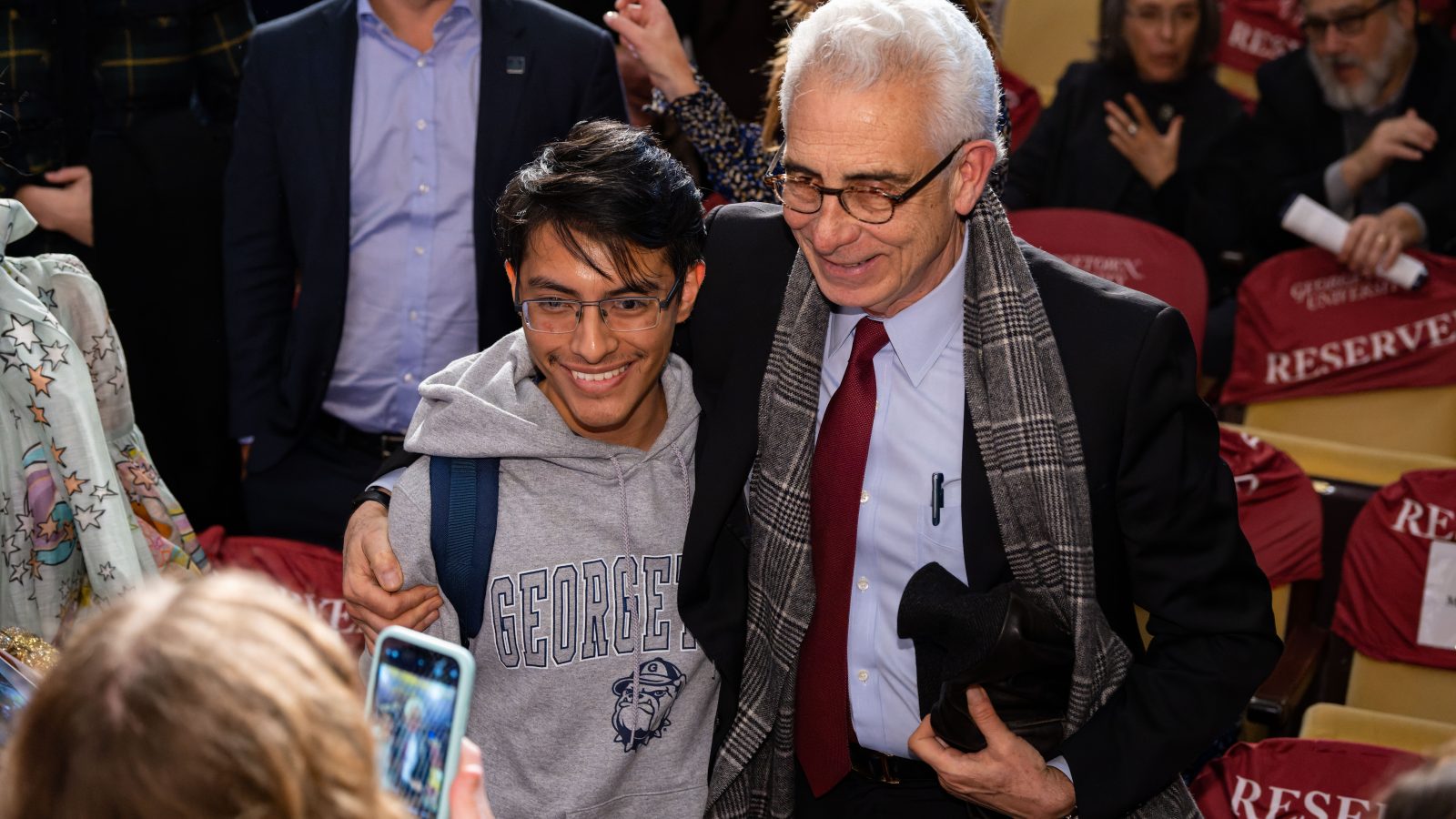 A former Latin American president (right) dressed in a black suit and red tie poses for a picture with a Georgetown student (left) wearing a gray sweatshirt that says &quot;Georgetown.&quot;