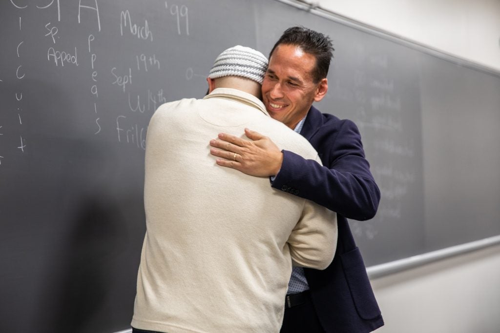 Marc Howard, director of the Prisons and Justice Initiative (PJI), hugs Adnan Syed, a program associate in PJI, in front of a chalkboard.