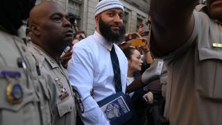 Adnan Syed leaves the courthouse after being released from prison Monday, Sept. 19, 2022, in Baltimore. He wears a white button-down shirt and a tie, and carries a binder with a Georgetown bulldog sticker on it.