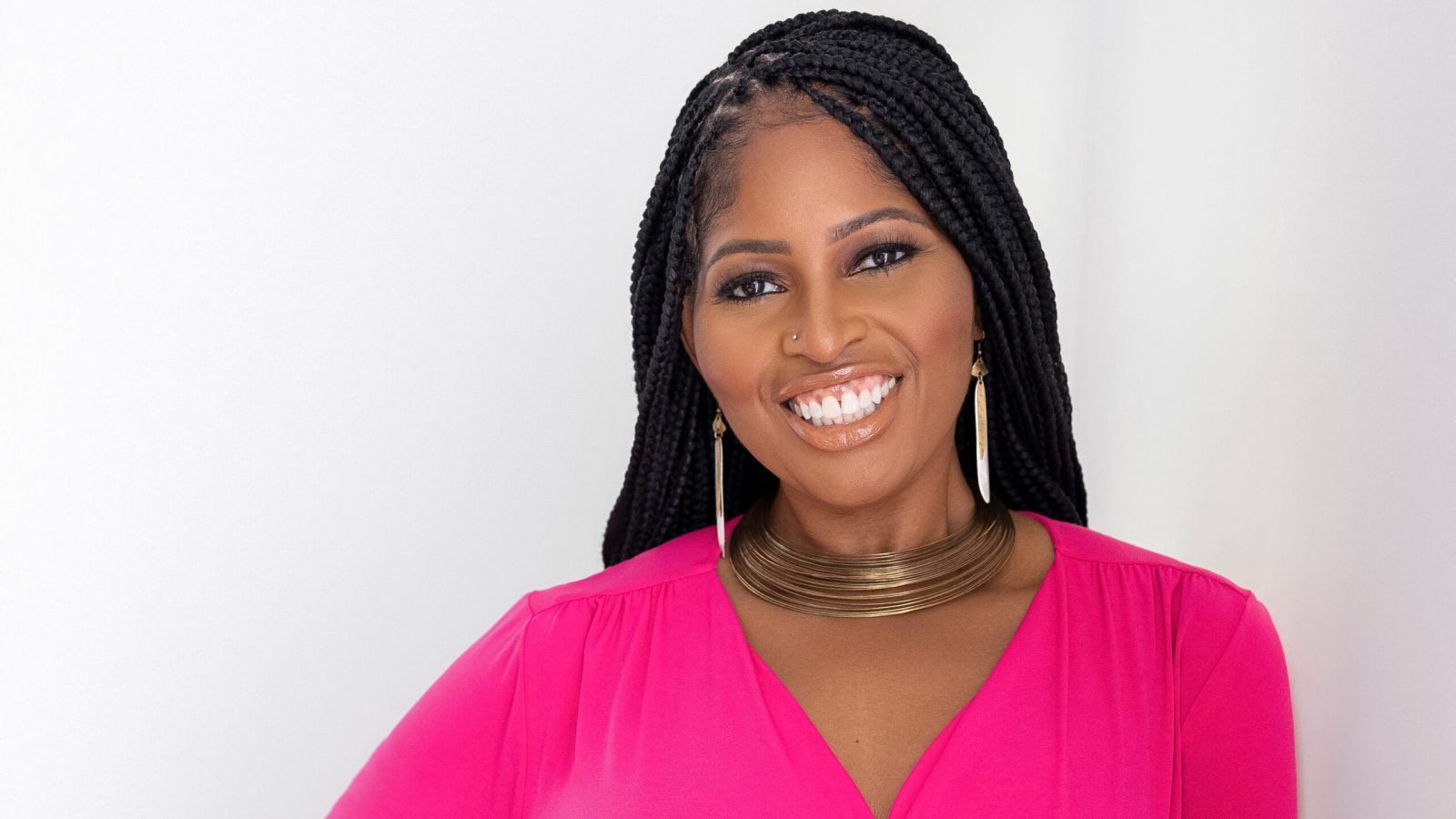 Woman wears a pink shirt and gold necklace against a white backdrop