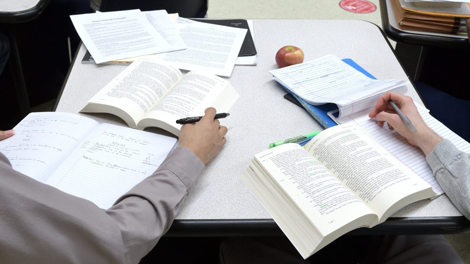 An image of five books open on a table while students study them.