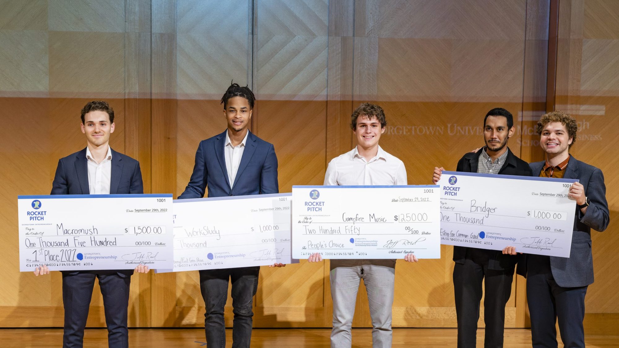 Student winners in pitch competition, holding large checks.