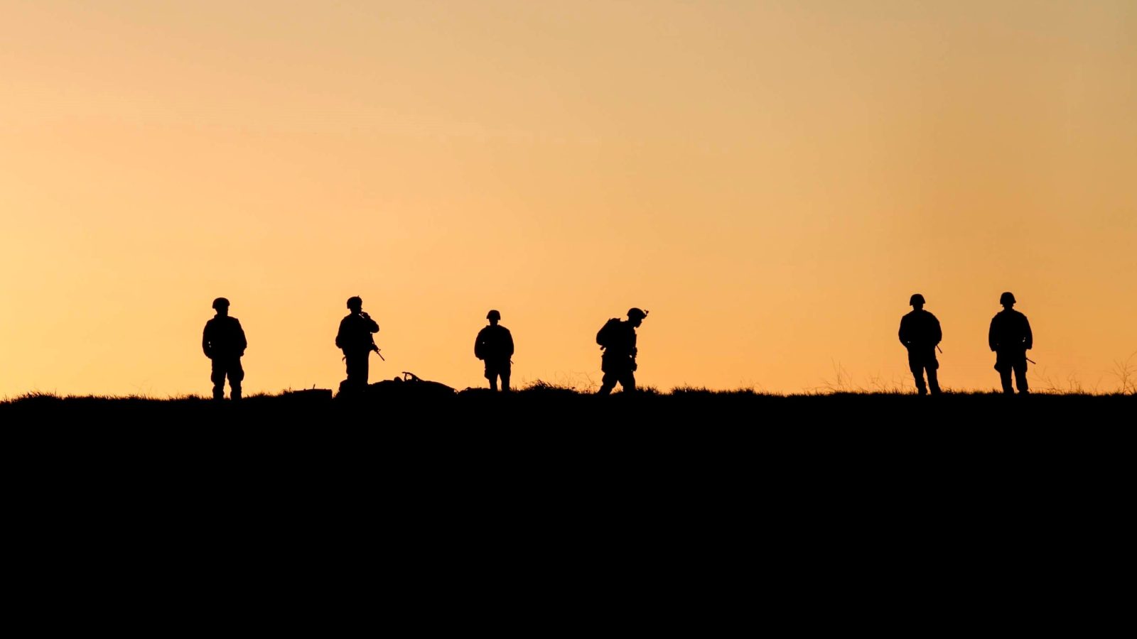 A group of uniformed soldiers stand silhouetted against a sunset