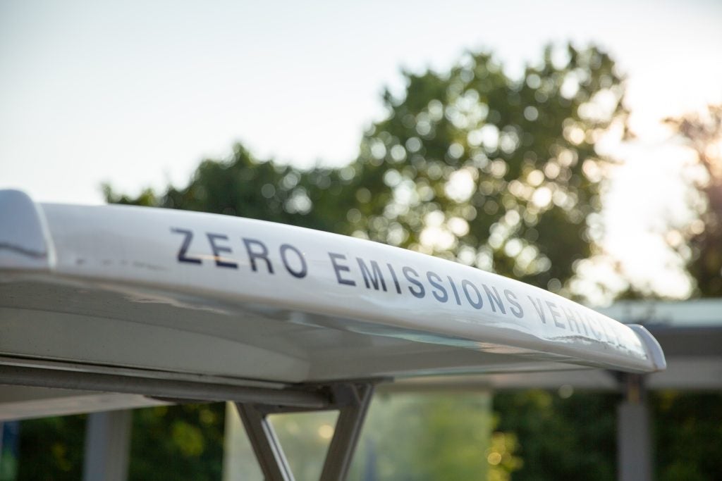 An image of the top of an electric golf cart that says "Zero Emissions Vehicle" across the front of the roof in all caps letters. Behind the close-up of the golf cart is the outline of a tree.