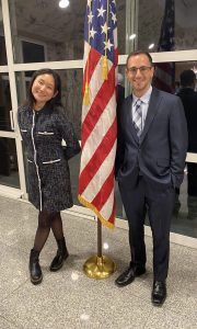 Breslow (SFS’22) (right) pictured at a reception with Mary Mei (C’20) (left), who is also teaching English in Poland. They are both dressed in formal wear. In between them is an American flag wrapped around a pole.