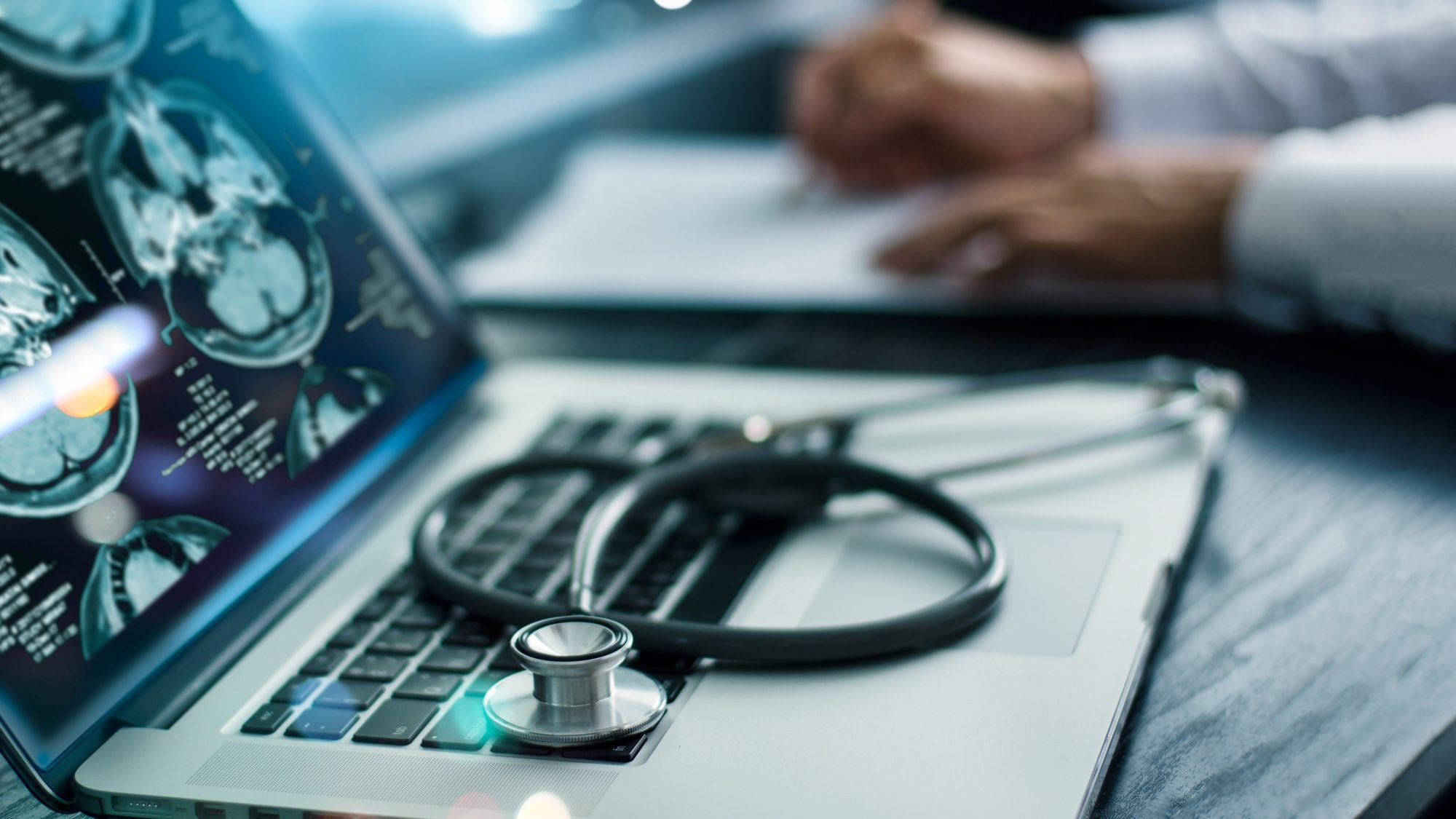 A close up of a laptop screen with brain scans and a stethoscope lying on the keyboard.