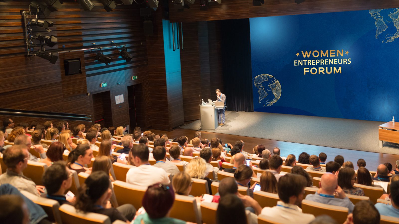 Person standing at podium in auditorium with WEF logo in background.