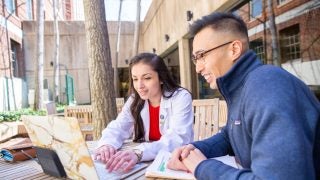 Two medical students look at a laptop at a table outside.