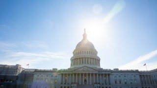 An image of the U.S. Capitol on a bright blue day. The sun illuminates the dome of the building.