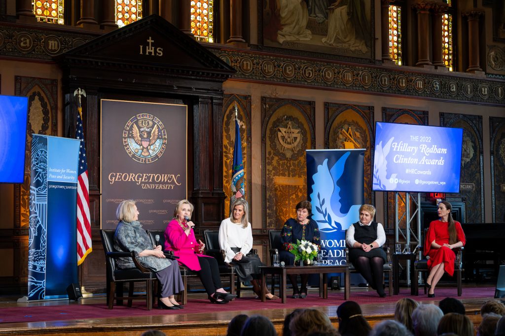 A panel of six people sit on stage in Gaston Hall. Speakers include Hillary Clinton and Sophie, Duchess of Edinburgh.