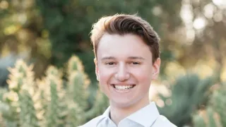 Brendan Foody (B&#039;25) smiles with arms crossed against a background of plants.