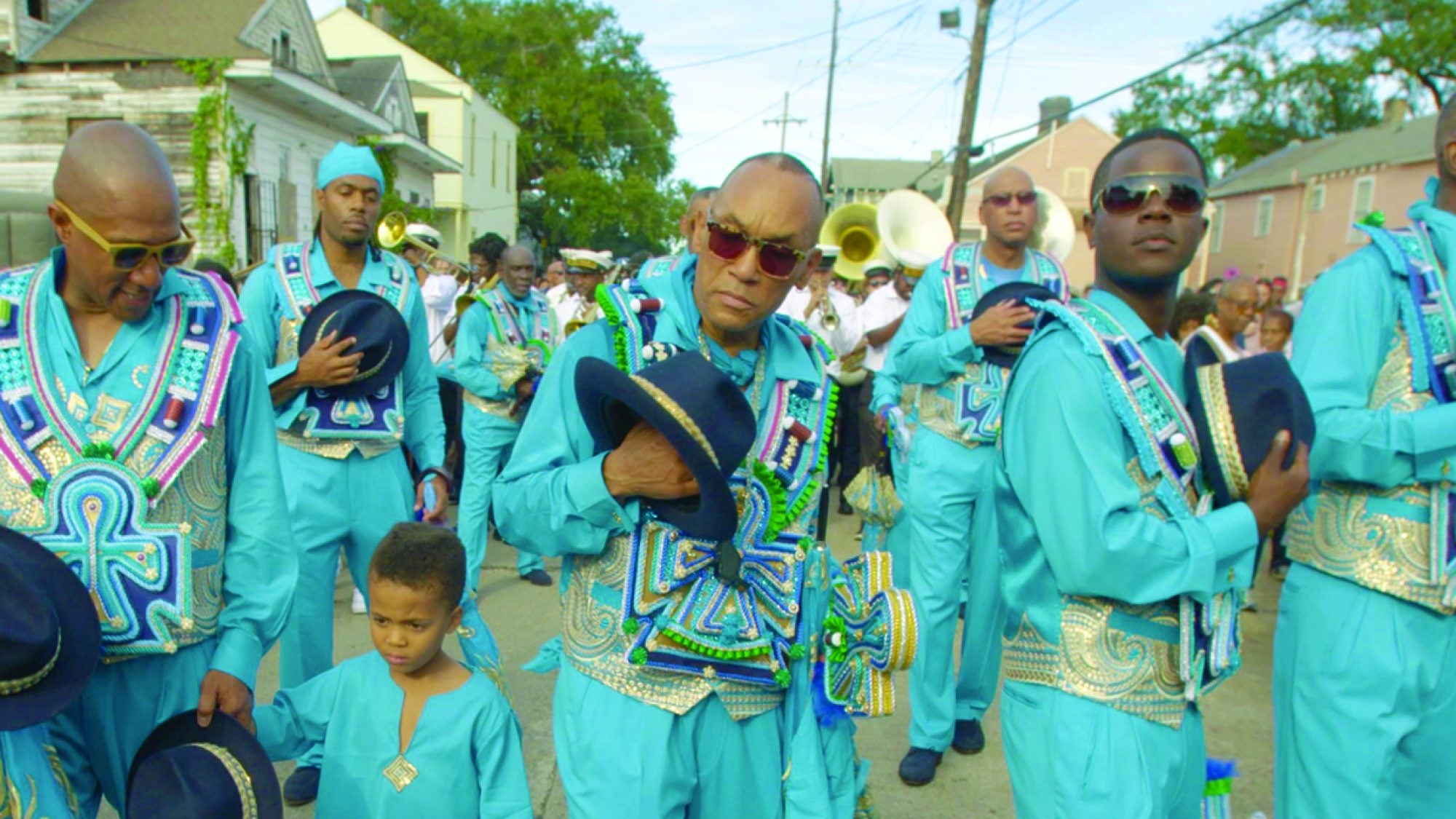 Still from City of a Million Dreams, individuals in teal suits on street.