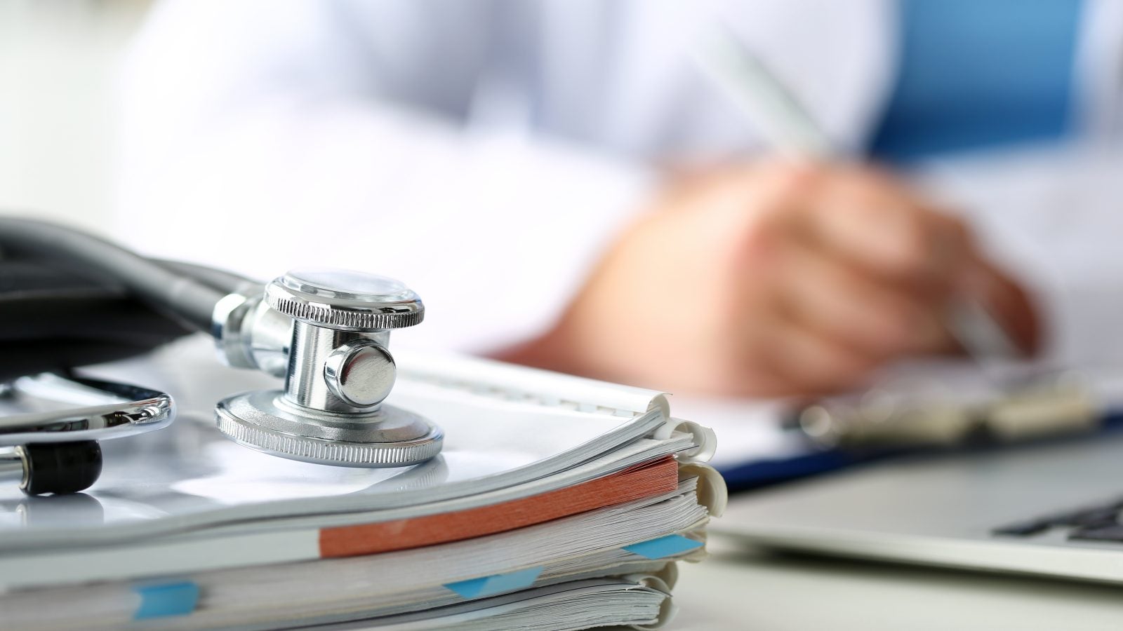 A stethoscope lies on a stack of notebooks and books